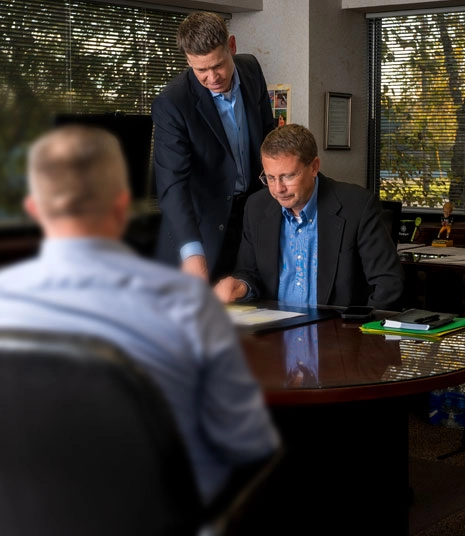 Three professionals seated around a conference table reviewing documents during an office meeting.